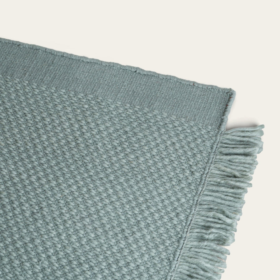 Textured teal blanket with frayed edge on a light gray background #sagegreen