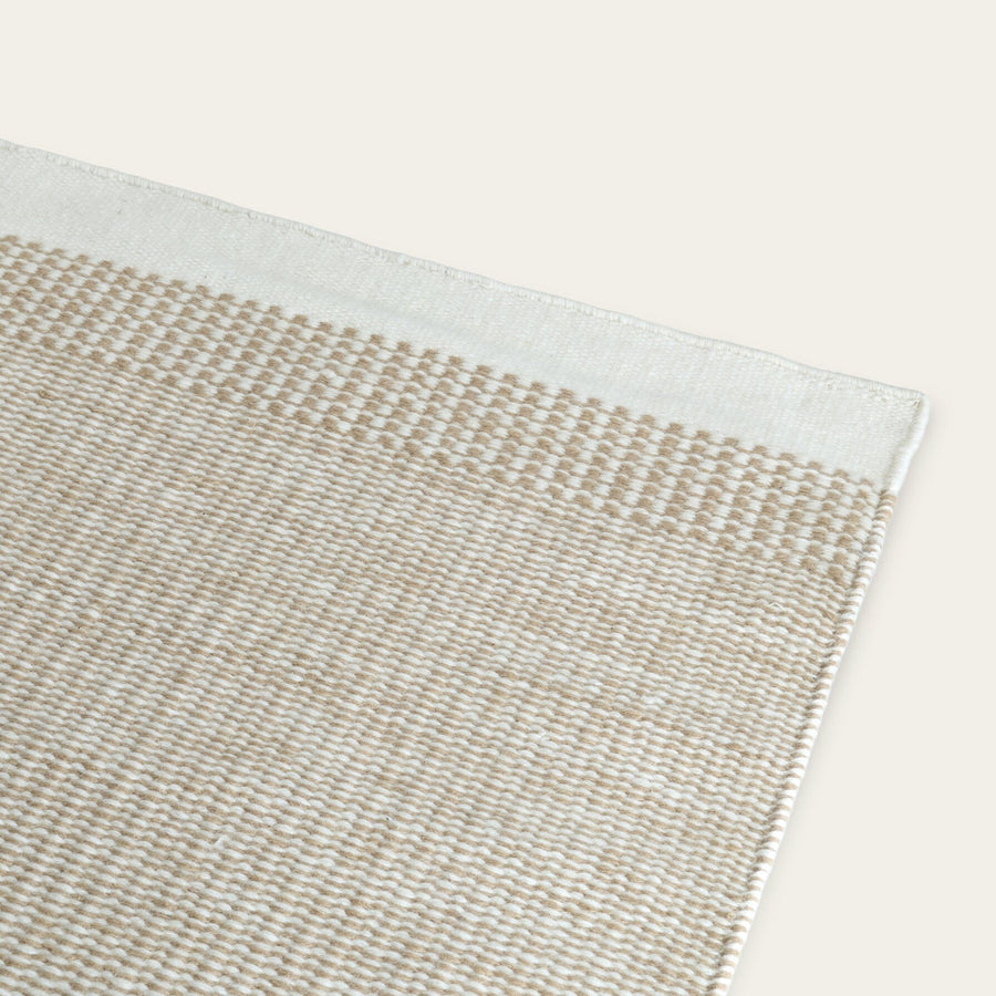 Close-up of a woven rug with a beige and white pattern on a light gray background #coastalcream
