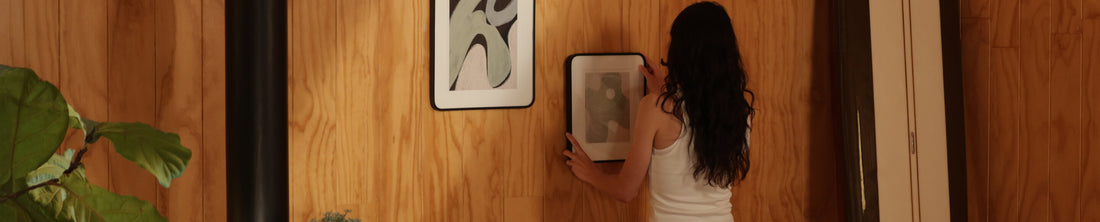 Woman hanging a framed abstract print on a wood-paneled wall