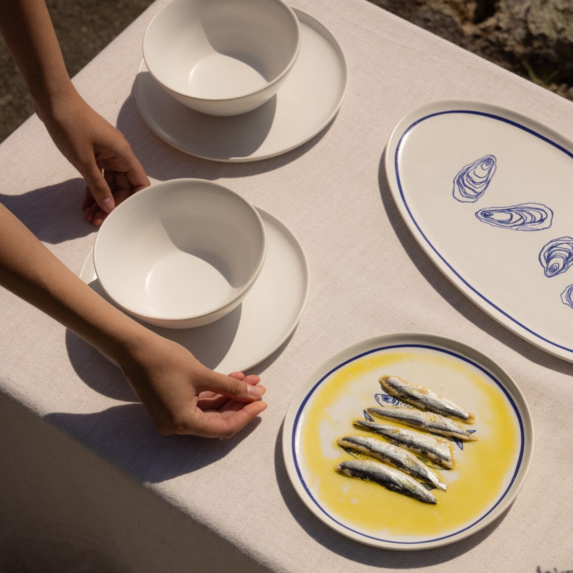 Person setting a table with white bowls and a plate of fish on a textured surface.