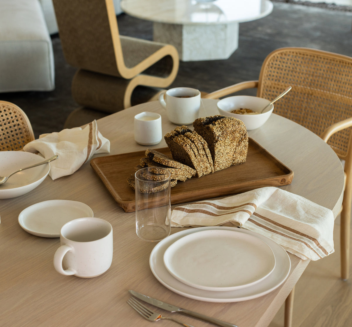 Fable white stoneware plates, mugs and bowls set on a wooden breakfast table with sliced seeded bread