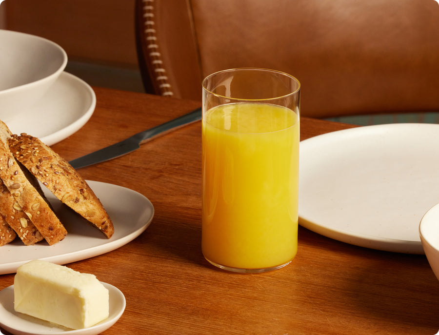 Fable clear tall highball glass of orange juice on a wood breakfast table with bread and butter