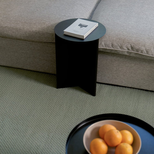 Black side table next to a beige sofa with a book on top, and a bowl of oranges on the floor. #sagegreen