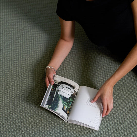 Black side table next to a beige sofa with a book on top, and a bowl of oranges on the floor. #sagegreen