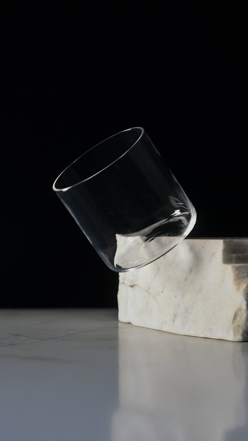 Clear glass tumbler balanced at an angle on a white marble block against a black background