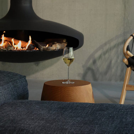 Glass of white wine on a wooden table in front of a modern fireplace. #clear