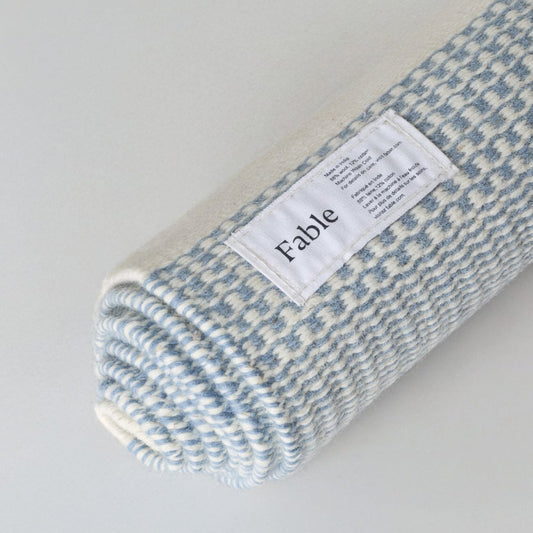 Folded blue and white checkered blanket with a label on a light gray background #duskblue