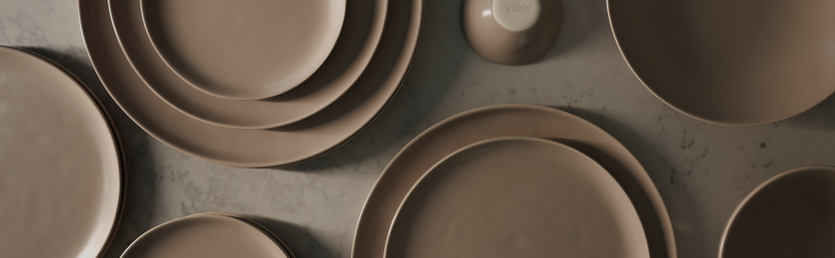 Terracotta-brown Fable stoneware plates and bowls arranged in a flat-lay on a grey surface