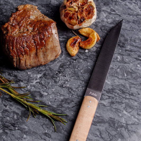 Steak, garlic, and a knife on a dark surface with 'Fable' branding. #natural