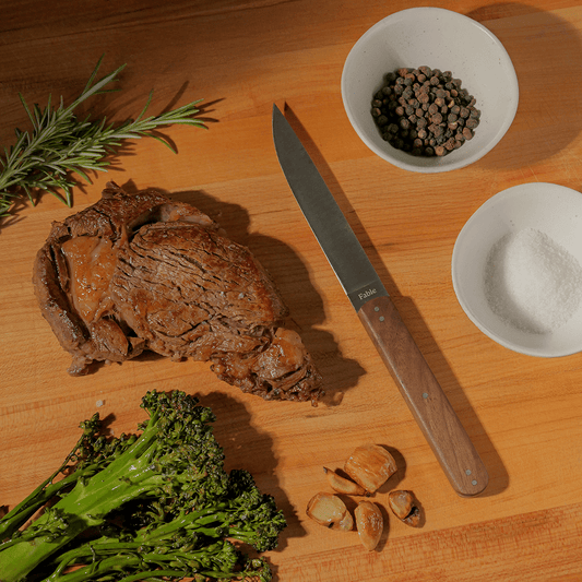 Meat, knife, and vegetables on a wooden cutting board with salt and pepper bowls. #walnut