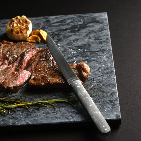 Sliced steak on a dark marble slab with a knife, garlic, and rosemary. #black