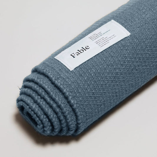 Rolled-up Seaside blue rug with a 'Fable' label on the gray  background. #seasideblue