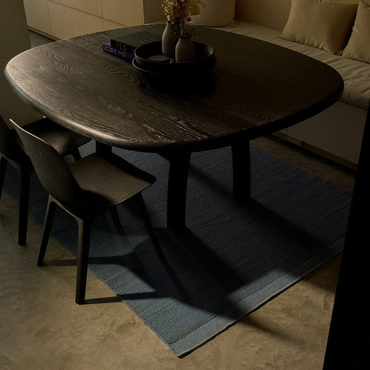 Round wooden dining table with chairs in a dimly lit room. #seasideblue
